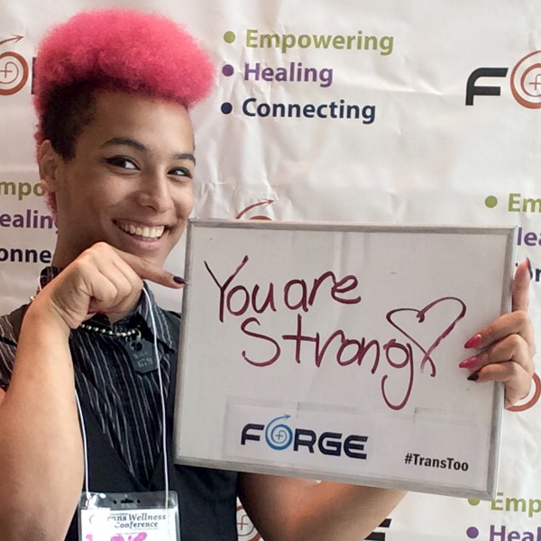 Photo of person with pink hair in front of FORGE logo background holding a sign that says "You're Strong" with a heart.