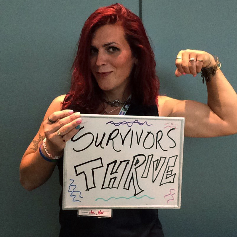 One smiling person flexing their bicep and holding a sign saying 'Survivors THRIVE"