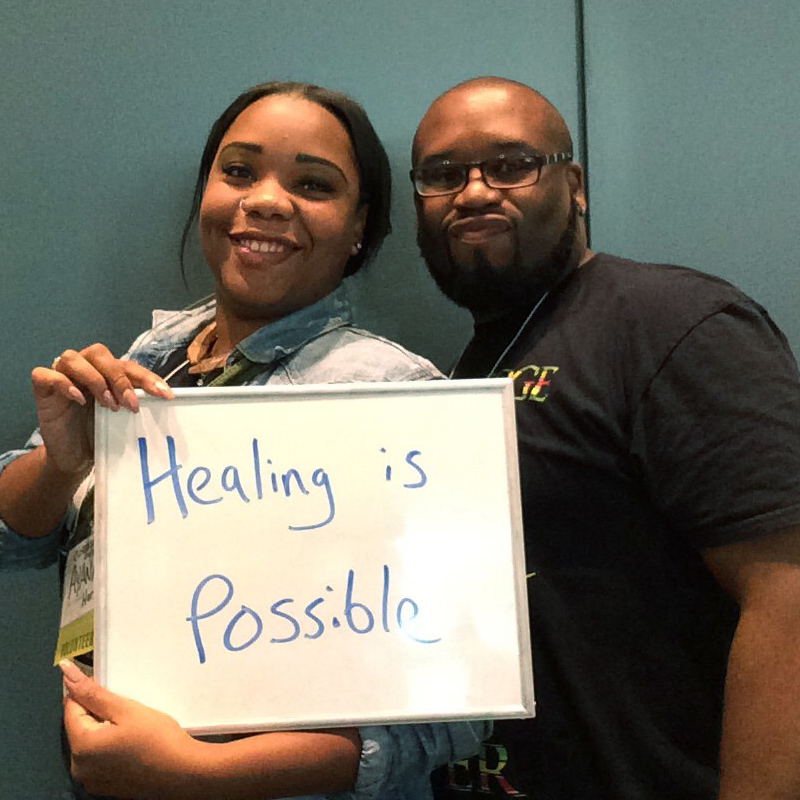two smiling people holding a sign saying 'Healing is Possible'