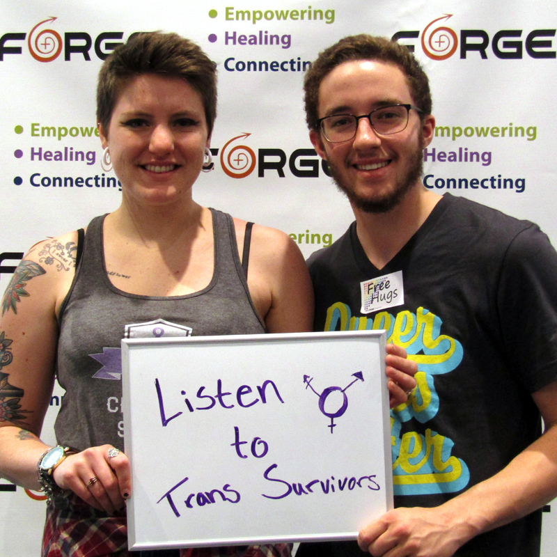 two smiling people holding a sign saying 'Listen to Trans Survivors' in front of a FORGE logo backdrop